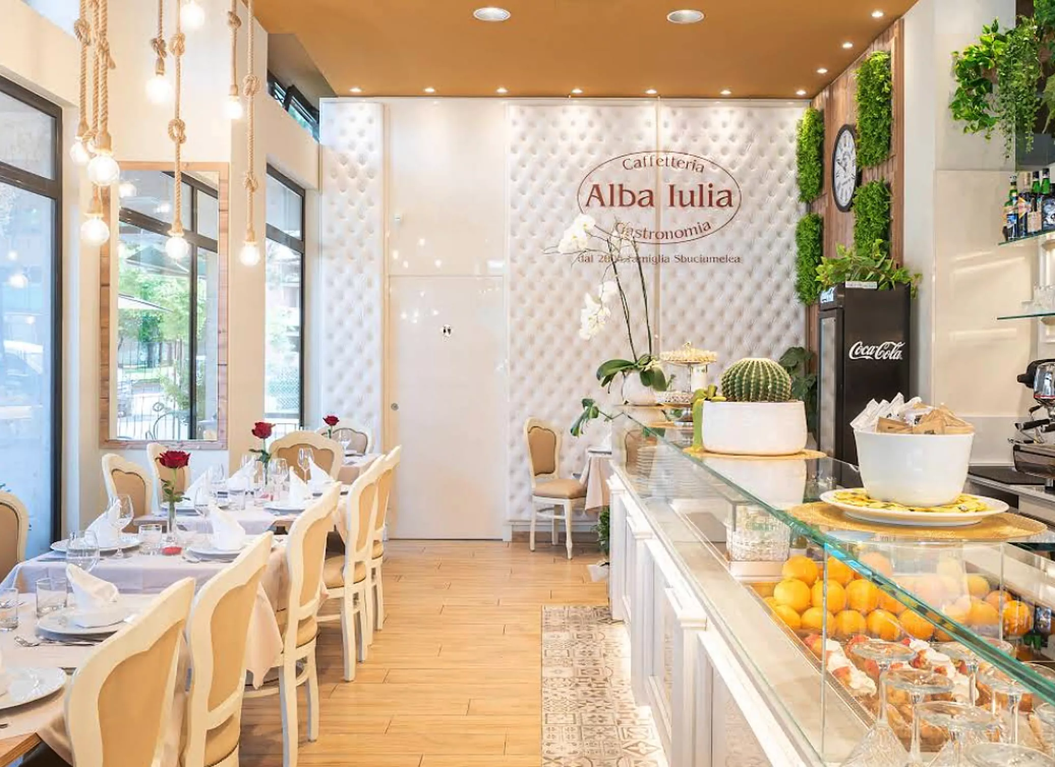 La sala di Alba Iulia: parete capitonné bianca con il logo, tavoli apparecchiati e il bancone della caffetteria